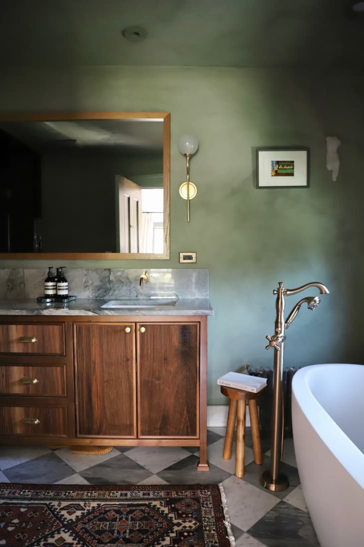 Green limewashed bathroom with wood and marble vanity.