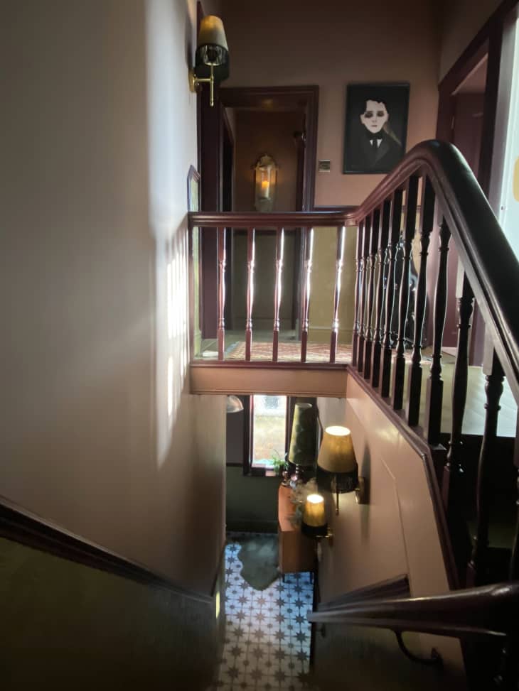 stairway looking down into front entryway with star pattern tile, wood railings, warm colored hallway with portrait on wall