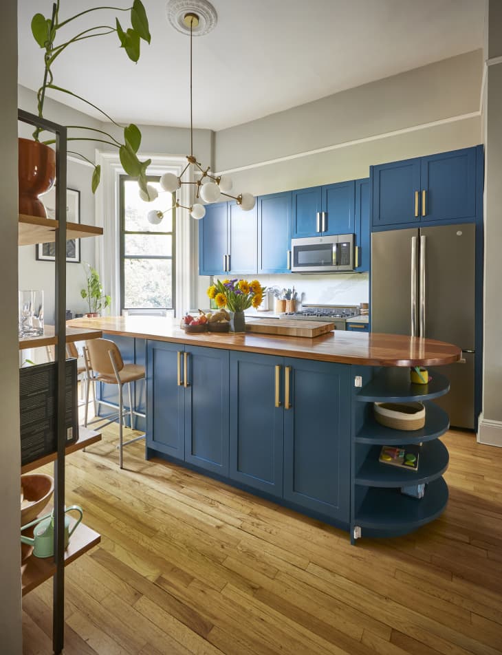 A gray-painted kitchen with blue cabinets, and stainless appliances in a studio apartment.