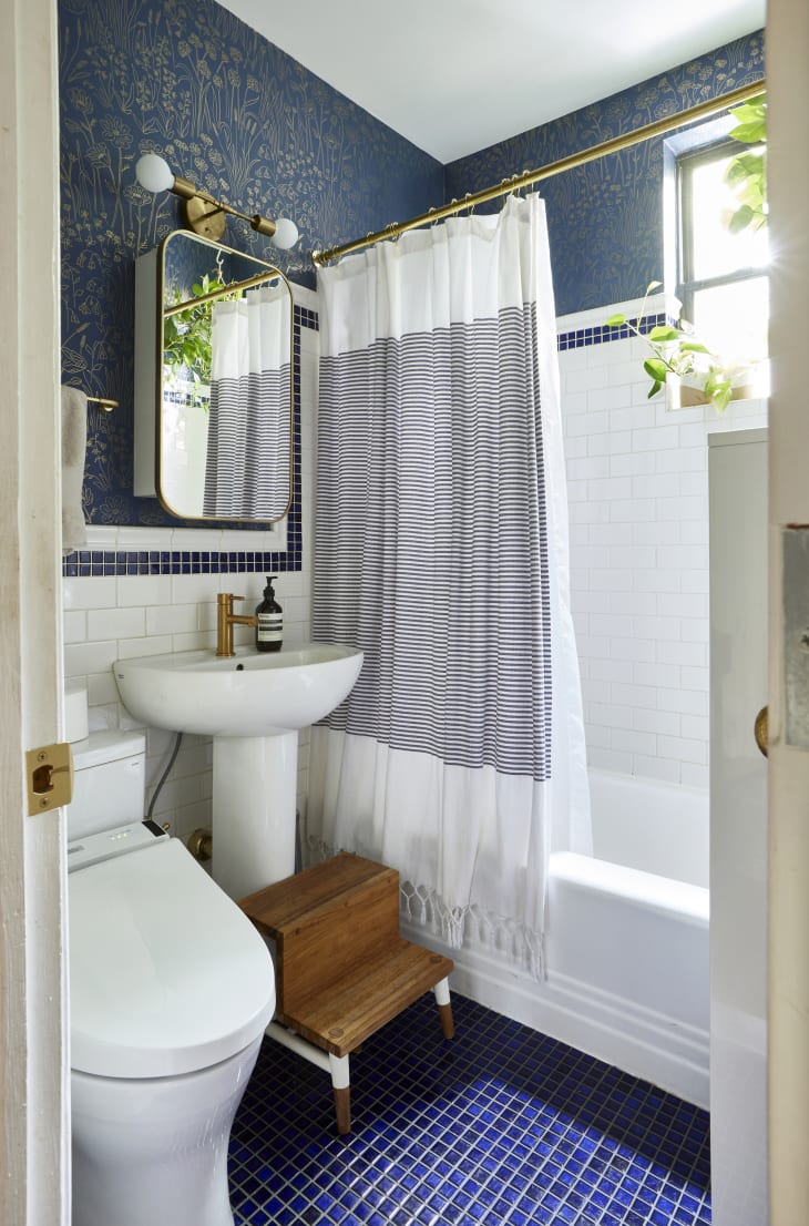 Blue and gold botanical wallpaper in bathroom with blue tiles and brass hardware.