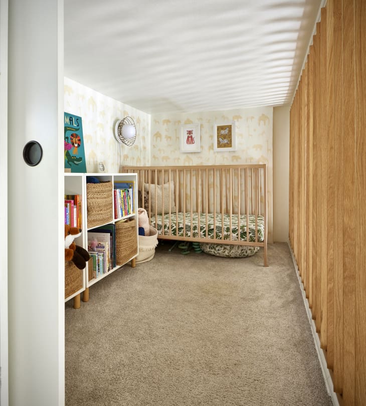 Animal-themed wallpaper in a child's nursery with a light wood crib and cubby storage.