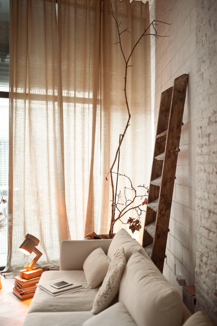 corner of white brick living room with off white sofa. large windows, and wood ladder