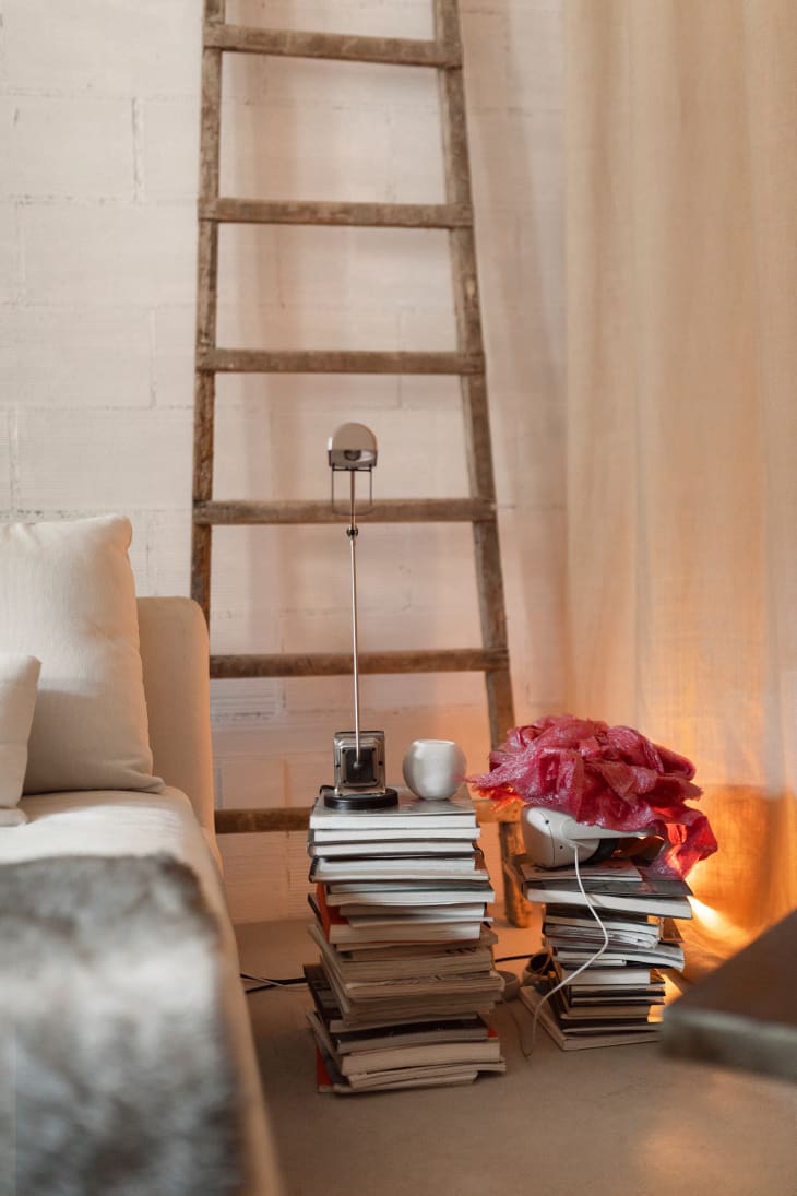 corner of white brick living room with stacks of books and a wood ladder