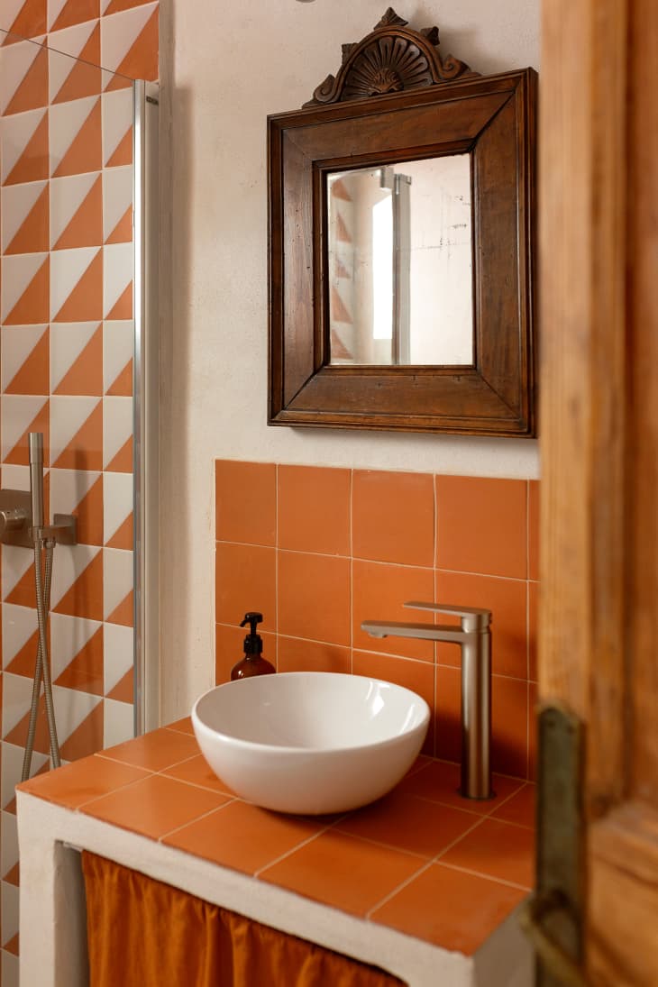 White bowl sink on top of orange, rust colored vanity.