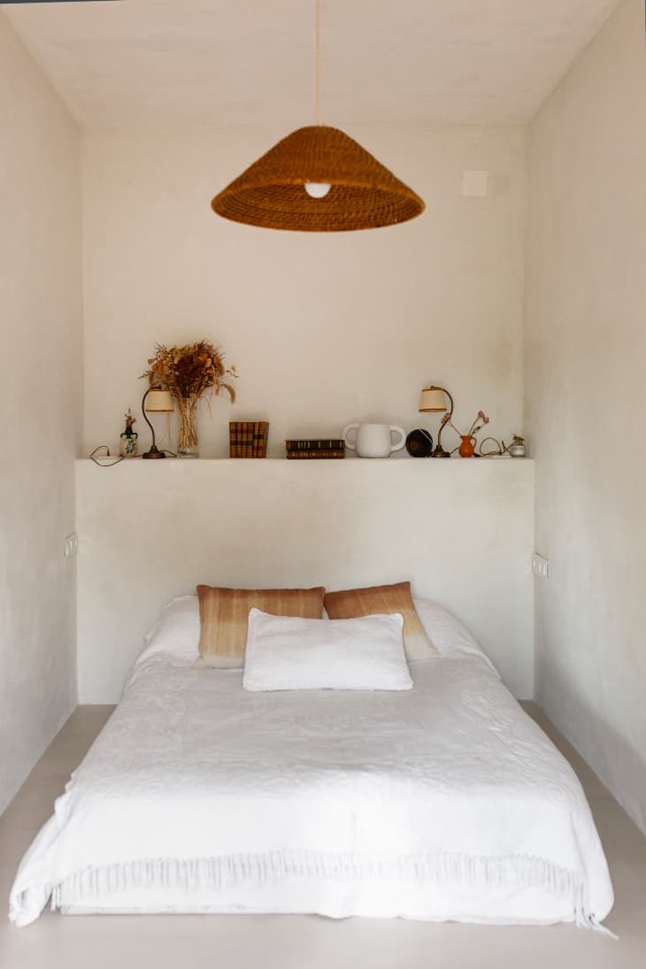 Wicker pendant over neatly made white bed.