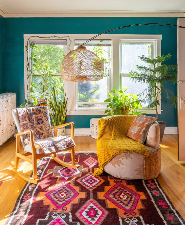 Teal sunroom with large windows, plants, and colorful boho decor elements