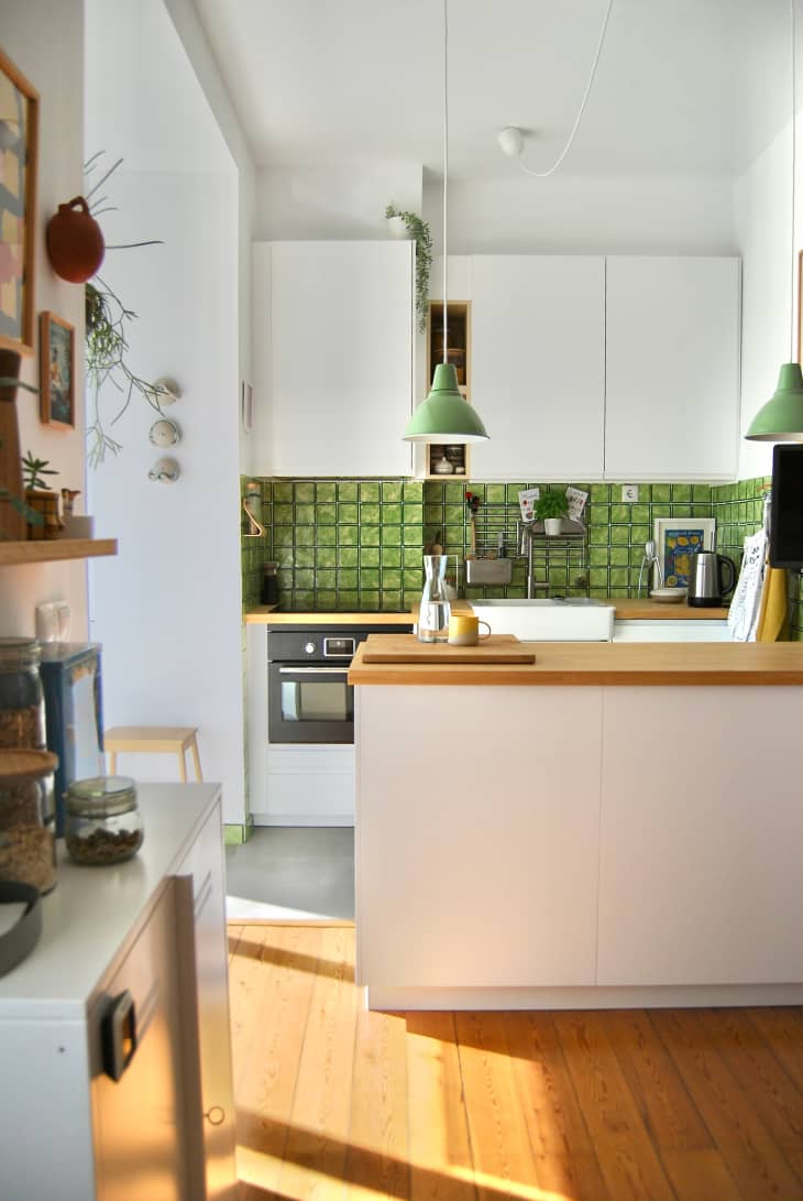 View of kitchen area with green backsplash and white cabinets.