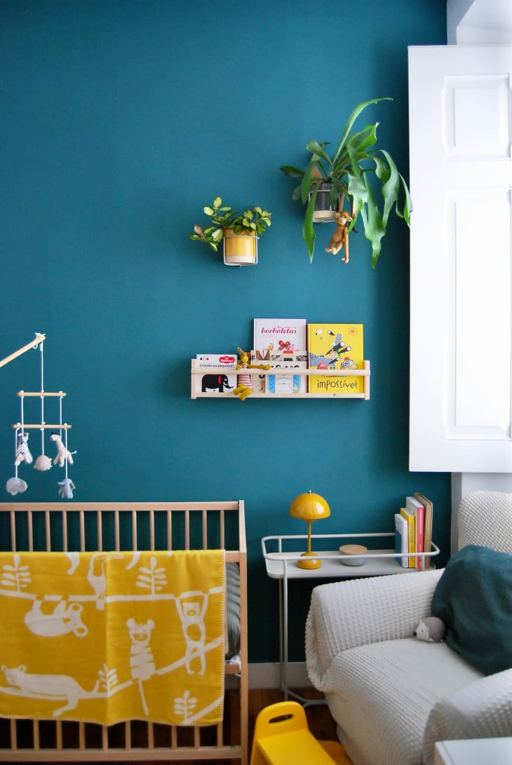 Corner view of teal nursery with books and plants.