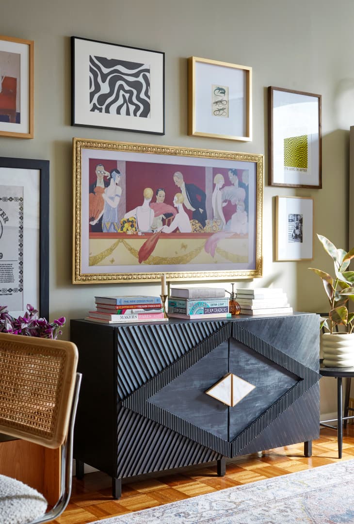 gallery wall over black credenza with textured geometric design. Books on credenza, dining chair visible