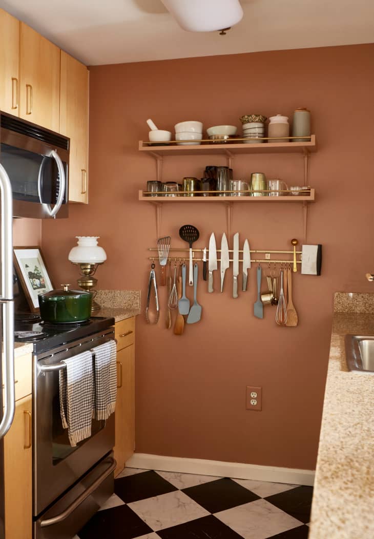 Kitchen with view of terra cotta colored wall with an organizer rack. wood cabinets and stove