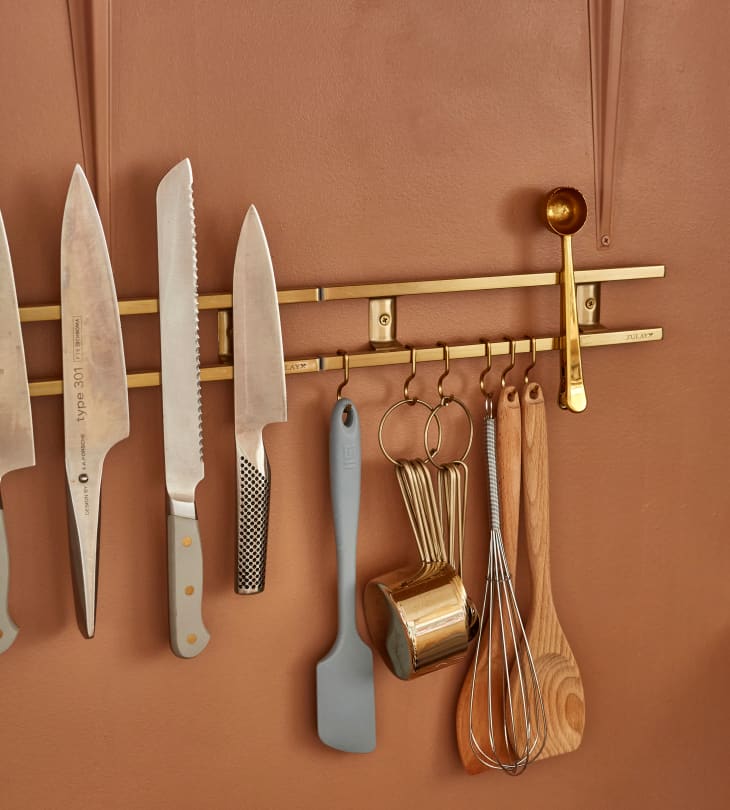 Racks on terra cotta colored kitchen wall with knives, utensils
