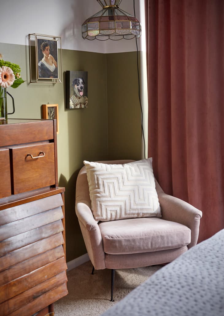 Coin de chambre avec fauteuil rose pâle. Pied de lit et partie de la commode vintage visibles. Murs peints à moitié en vert olive