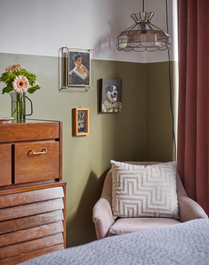 Corner of bedroom with pale pink armchair. foot of bed and part of vintage dresser visible. Walls painted halfway with olive green