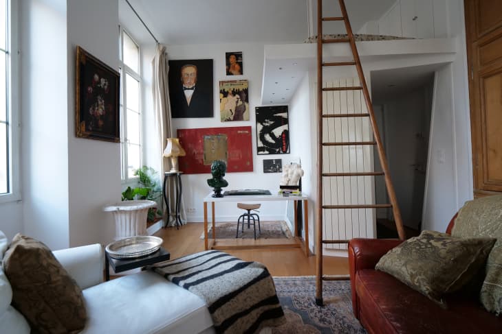 living room. White walls, wood ladder up to loft, large paintings, rust leather sofa, art objects