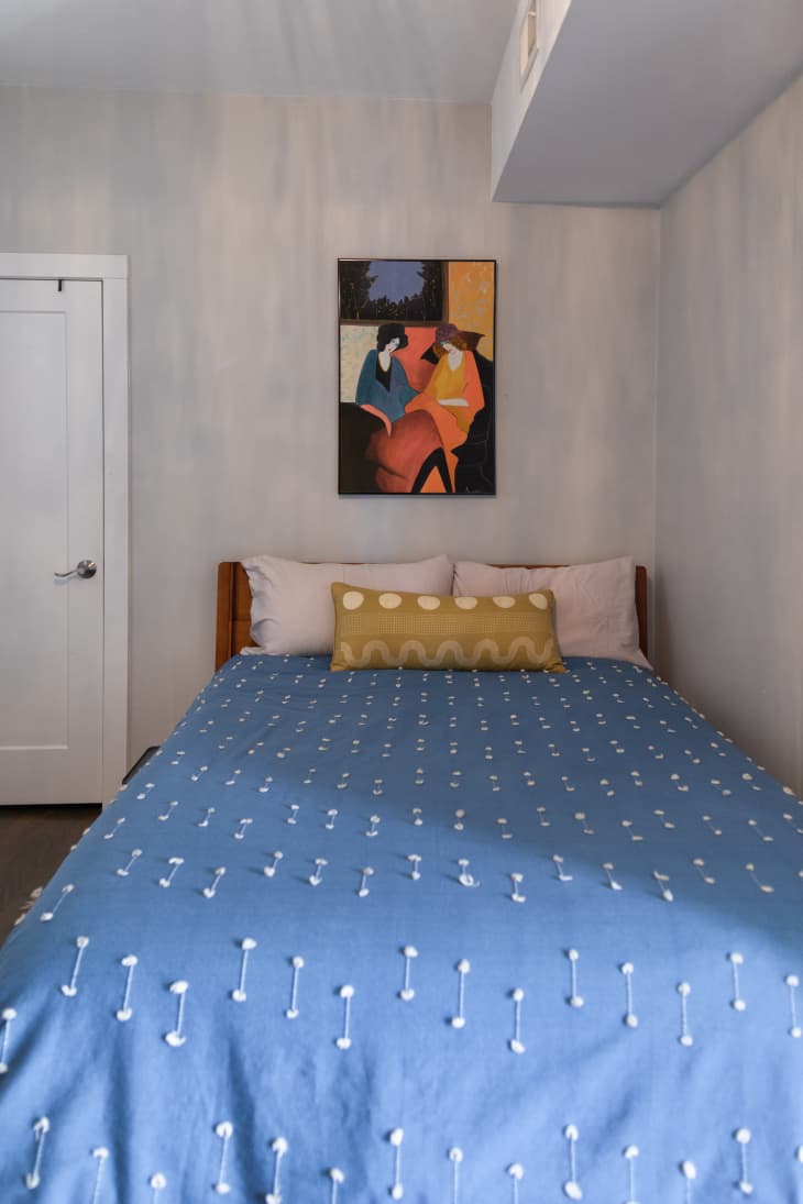 A bed with a blue and white duvet and a painting hanging above