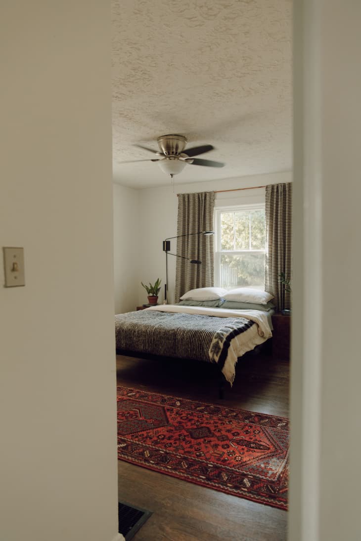 A bedroom with a large bed, ceiling fan, and open curtains