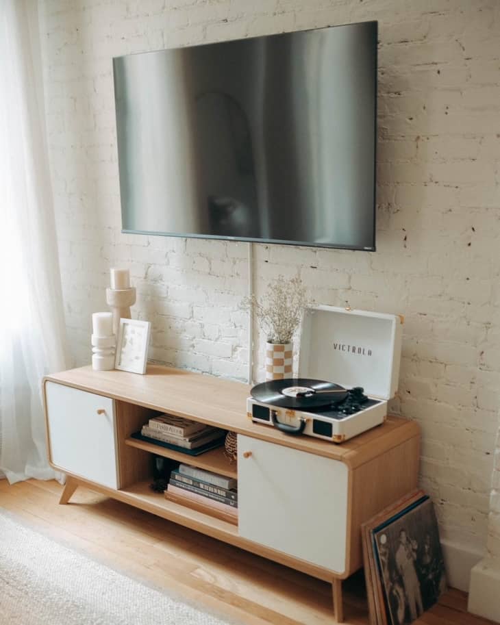 A wooden TV console under a TV by a white brick wall