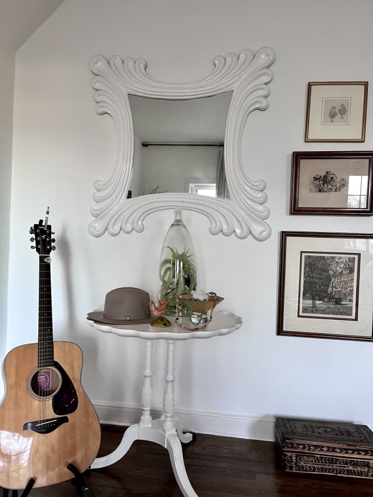 A white wall with a mirror, guitar, and framed photos
