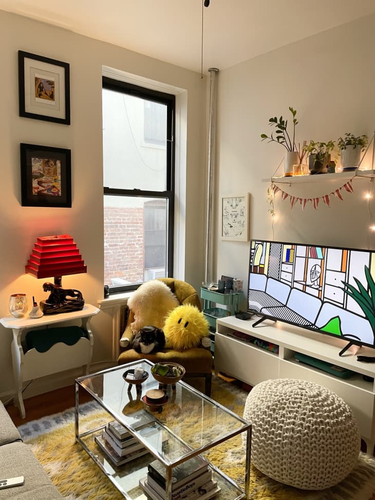 Brooklyn apartment filled with stuffed pillows and a red lamp on small table.