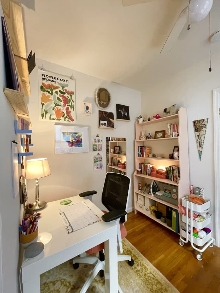 Office space in apartment with shelving and floral poster hanging on wall.