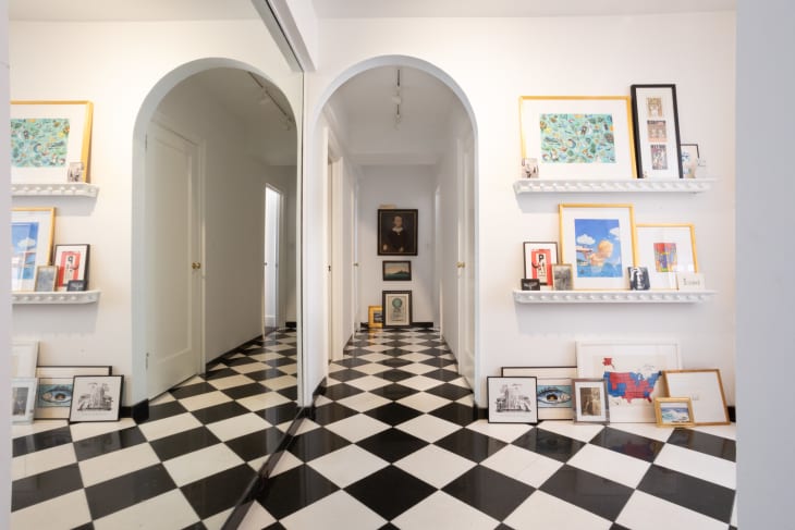 Archway leading to front entryway. Mirrored wall on left reflecting the room which has black and white checkered floor, framed art on built in shelves and on floor