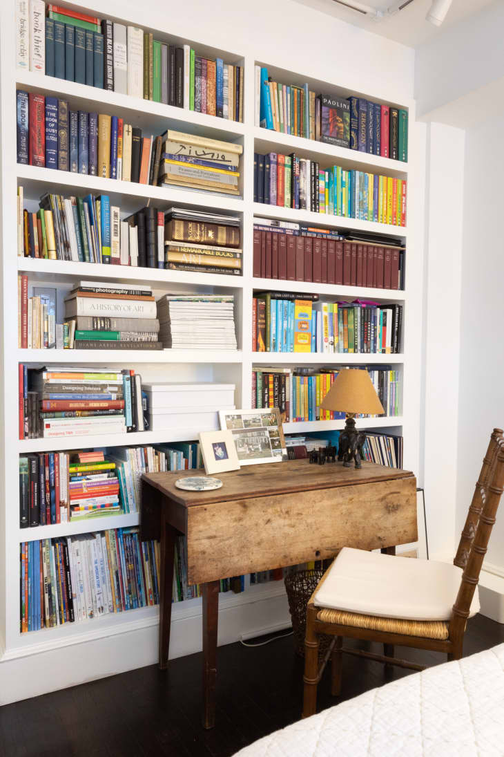 white built-in bookshelves full of books, rustic wood desk and chair
