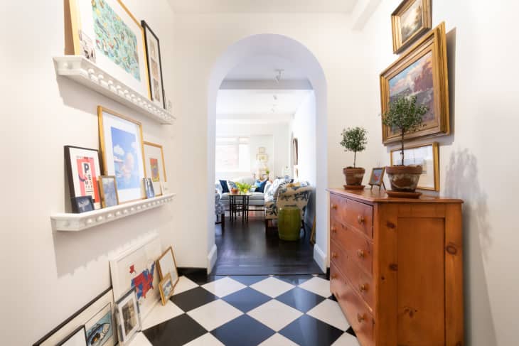 hallway area with black and white checkered floor, arched doorway, wood dresser, art on built-in shelves. Living room visible through arch