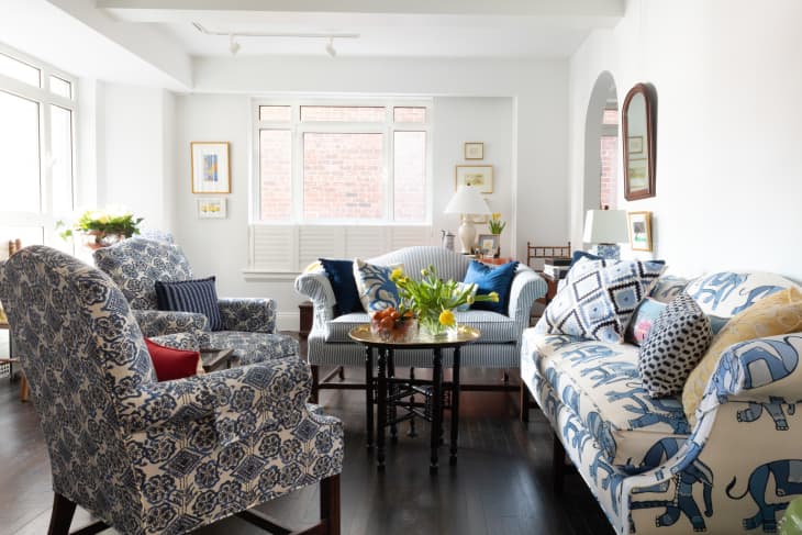 Living room with blue and white patterned sofa and accent chairs, white walls, dark wood floor. coffee table with fresh tulips in vase