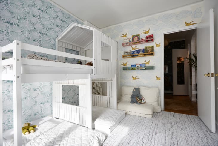 Light colored kids bedroom with bunk bed and a reading nook with hanging book shelves and pillows on the floor.