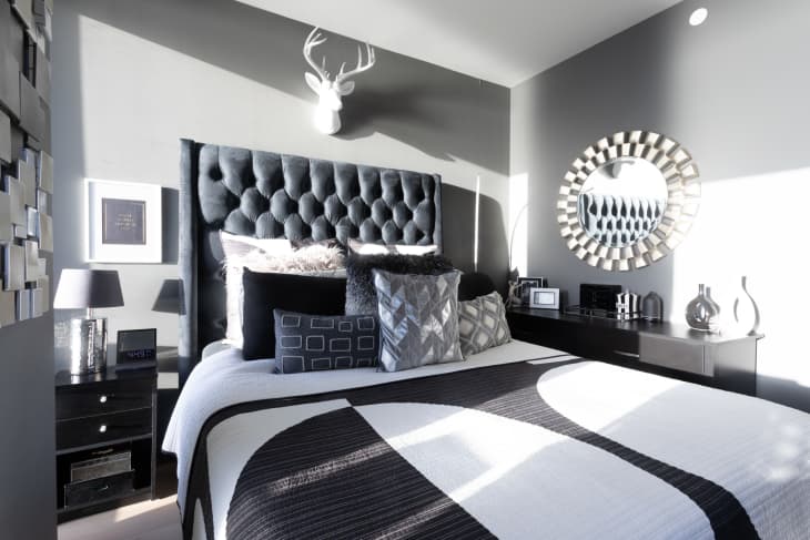 Bedroom with lots of black, white, and gray. Graphic geometric linens, throw pillows. Tufted gray headboard