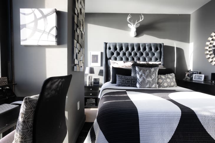 Bedroom with lots of black, white, and gray. Graphic geometric linens, throw pillows. Tufted gray headboard