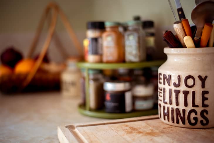 closeup of ceramic vessel full of utensils on counter that reads "enjoy the little things"