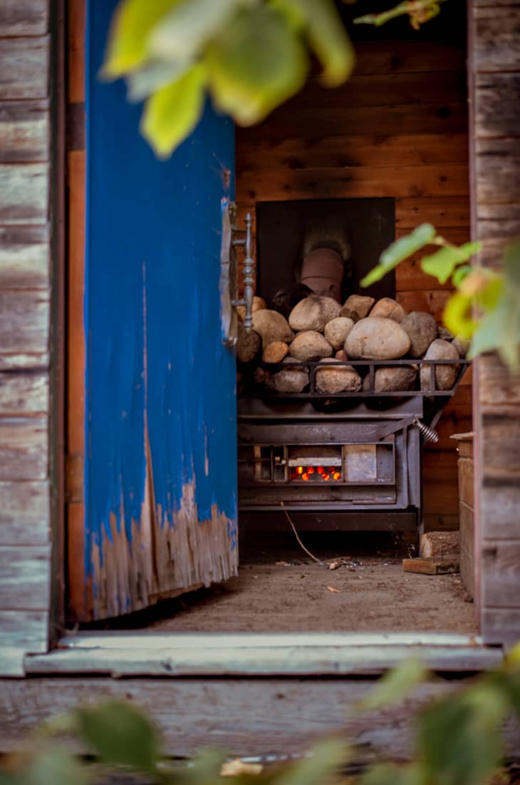 Blue door opening onto a sauna--we can see the stove with the hot rocks