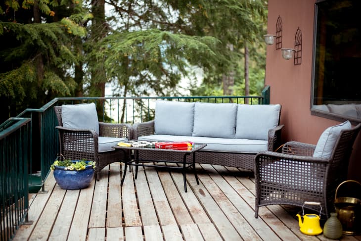 wood deck outdoors with gray sofa, coffee table. Large pine trees in background