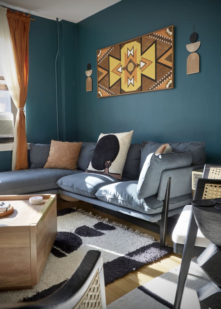 Detail of living room with teal walls, orange curtains, gray sofa, black and white are rug