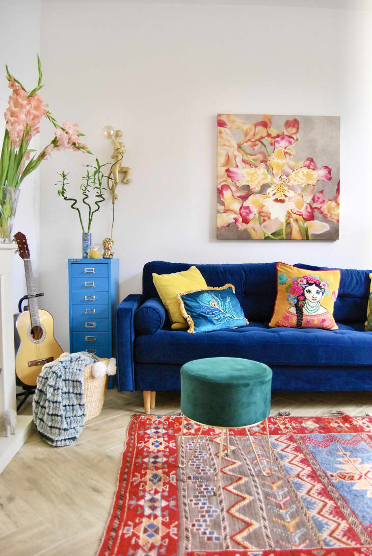 Colorful living room with blue velvet sofa, green ottoman, and yellow pillows.