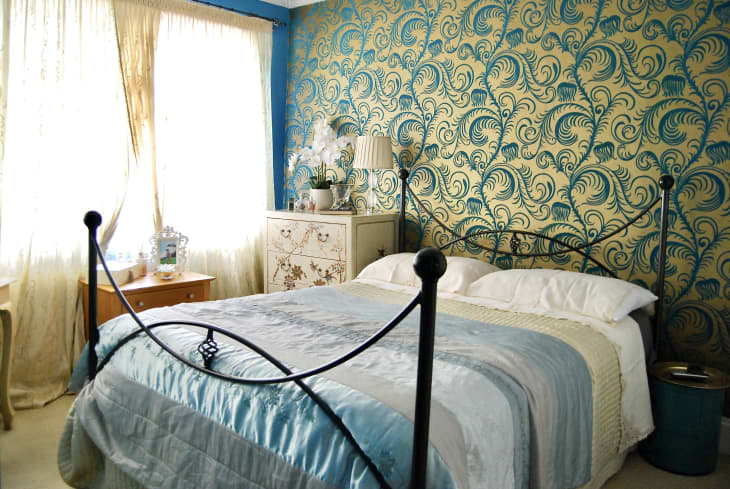 Gold and blue feather motif wallpaper in blue bedroom.
