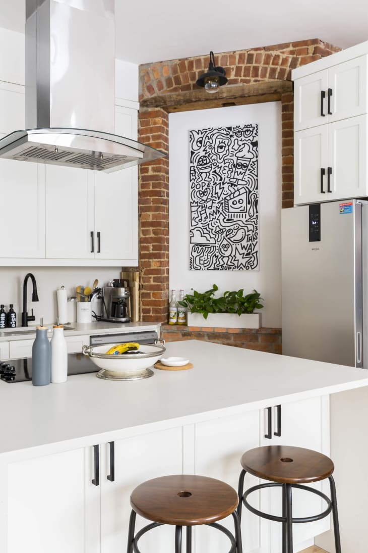A kitchen with white cabinets and a white island with an exposed brick wall