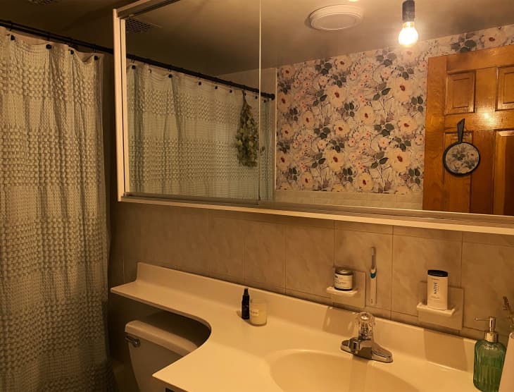 A bathroom with floral wallpaper and a rectangular mirror above the sink
