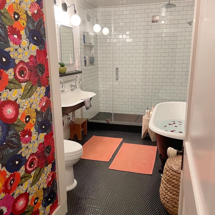 A bathroom with a separate shower and tub with two orange bathmats on the ground