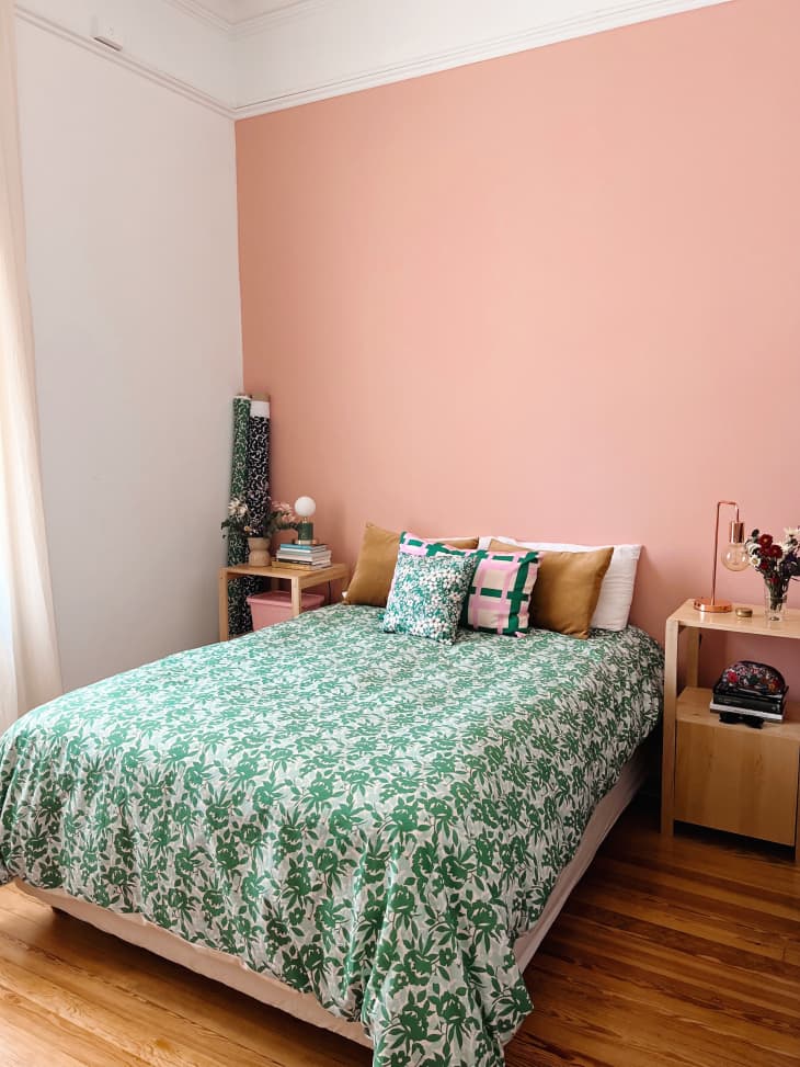 A pink bedroom with a green floral blanket on the bed