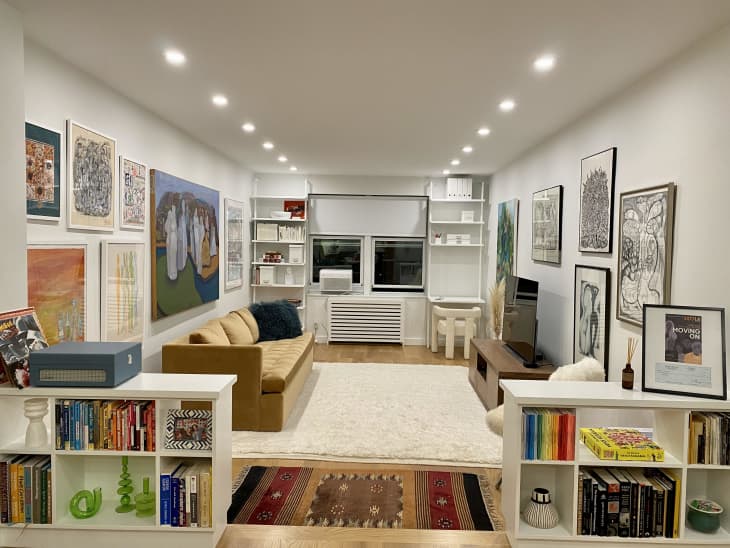 A white living room with framed art on the walls and two white bookshelves