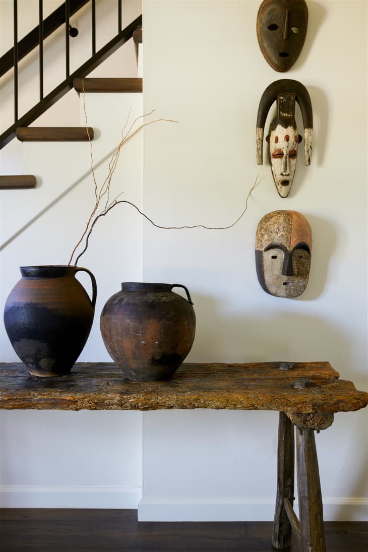 African masks on display in hallway with wooden table and vases.
