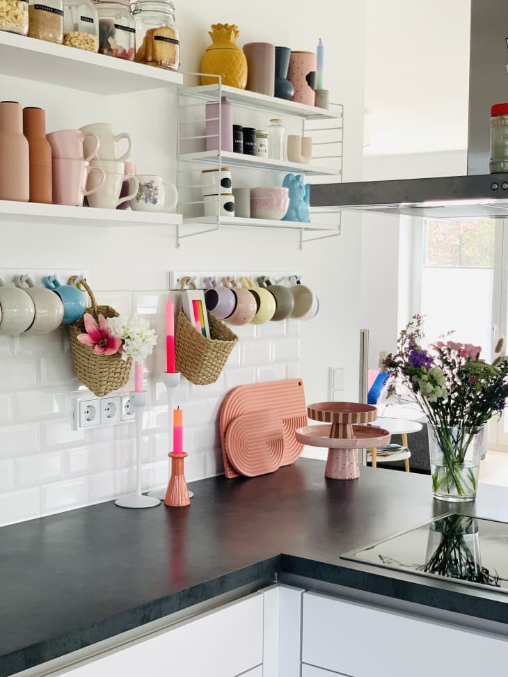 black counter top, white subway tile, colorful tea cups, open shelving, floating shelves, hood vent, flowers, airy, bright