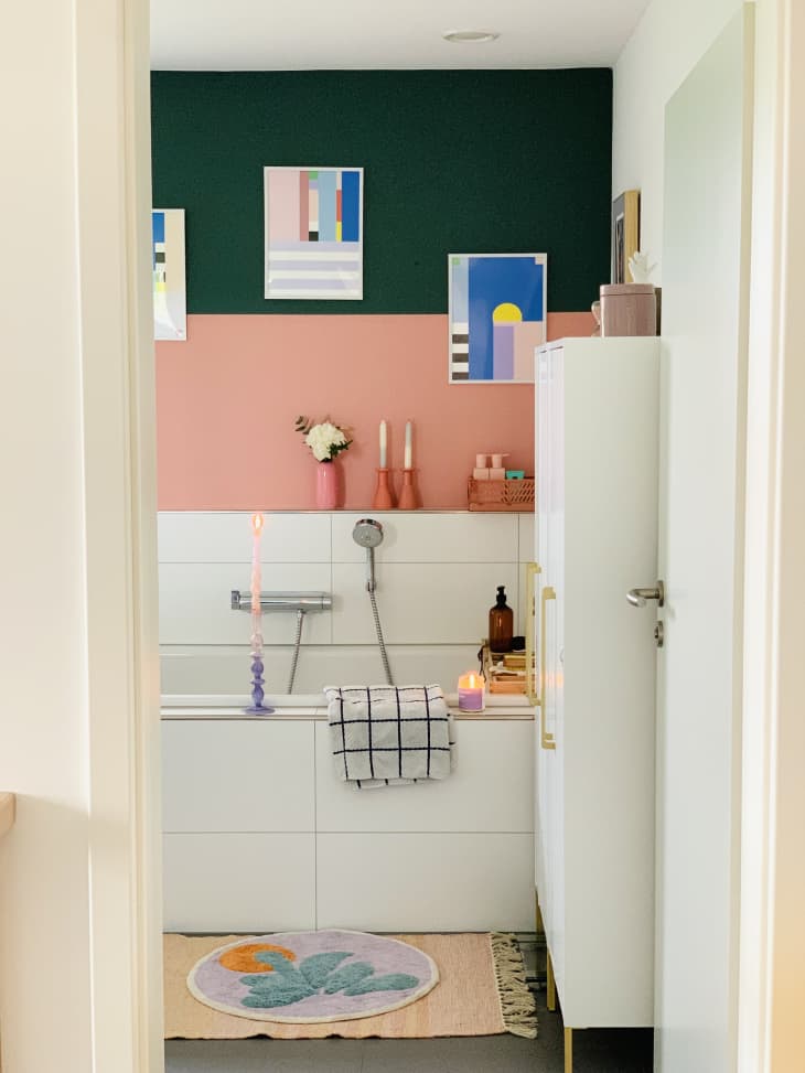 green and pink color blocking, white tub, hand held shower head, white cabinet, door frame, colorful art