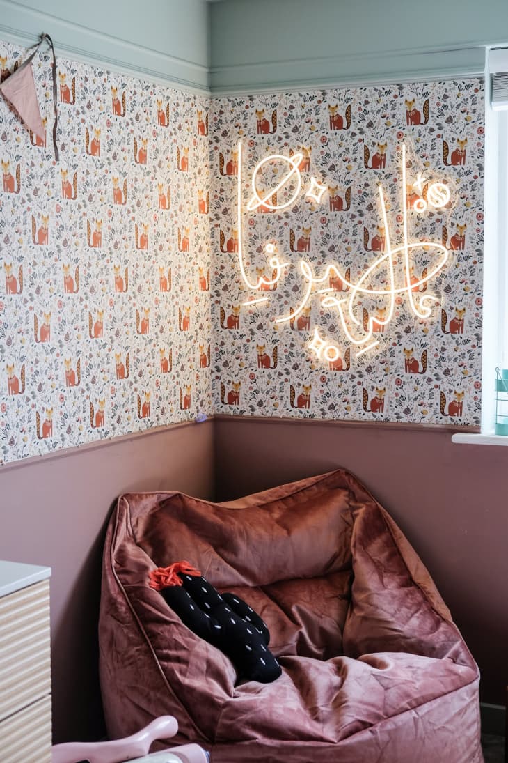 illustrated fox pattern wallpaper on half wall, dusty pink paint on bottom half of wall, dusty pink bean bag chair, blue ceiling, space themed neon light on wall