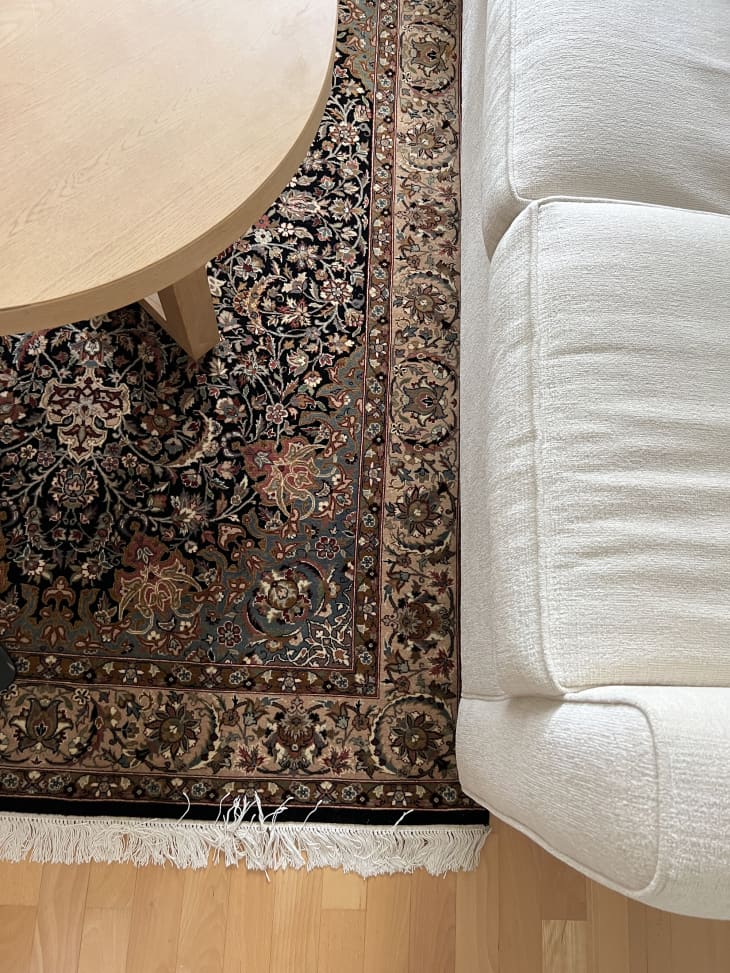 detail of brown persian area rug under white sofa, light wood coffee table