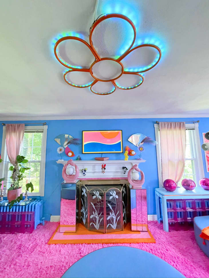 fireplace, blue walls, pink carpet, daisy neon lighting fixture, pik disco balls, plants, vintage fire guard