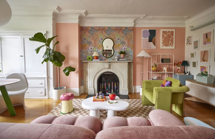 Peach/pink painted art filled living room with a section of floral wallpaper on wall with fireplace.