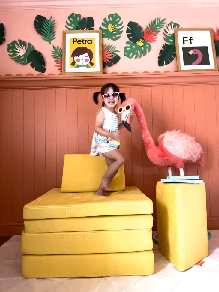 A chid poses in a renovated nursery with a large flamingo.